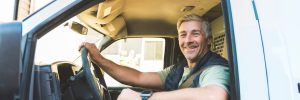 A happy temporary truck driver smiles from the cab of his truck