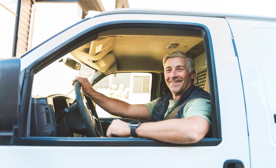 A happy temporary truck driver smiles from the cab of his truck